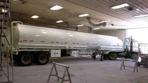 White tank truck parked inside a paint shop
