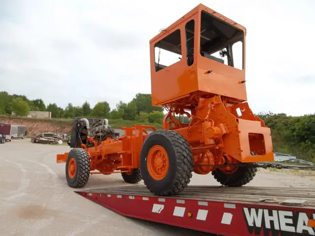 Orange road grader riding on a flatbed trailer