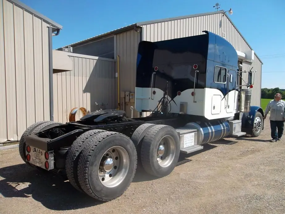 Rear of the blue and white Peterbilt tractor with a person standing at the right